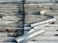 Zniszczone eternitowe pokrycie dachu, z widocznymi pęknięciami i fragmentami rur azbestowych.