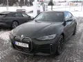 Zielony BMW i4 na ładowarce. W tle ciemny Porsche Taycan. Dane techniczne BMW i4 interesują wielu.