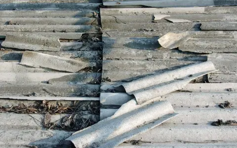 Zniszczone eternitowe pokrycie dachu, z widocznymi pęknięciami i fragmentami rur azbestowych.