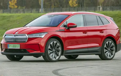 Czerwona Skoda Enyaq na tle zieleni, z tablicą rejestracyjną PY 00017. Ten elektryczny SUV oferuje imponujący zasięg.