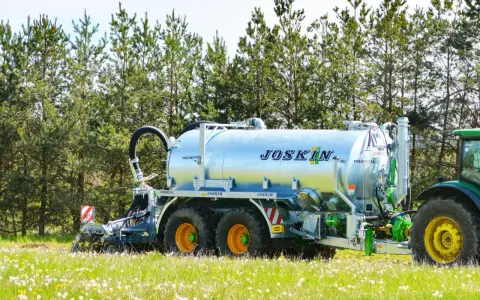 Cysterna JOSKIN na polu, gotowa do rozrzucenia gnojowicy lub gnojówki. Zielony traktor czeka w tle.