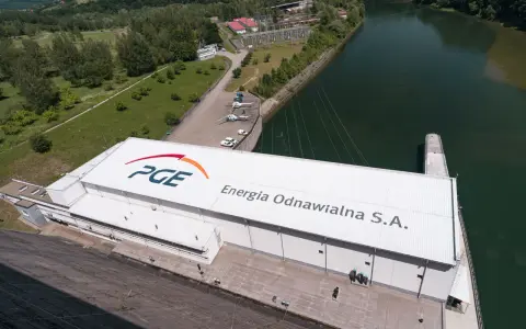 Widok z lotu ptaka na elektrownię wodną PGE Energia Odnawialna S.A. z charakterystycznym logo. Widać tam też helikoptery i samochody.