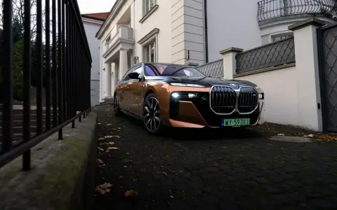 Eleganckie BMW i7 w miedzianym kolorze, zaparkowane przed willą. Ten luksusowy samochód elektryczny oferuje imponujący zasięg, pozwalając na długie podróże.