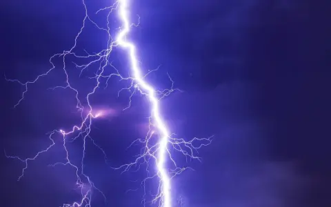 Potężne wyładowanie atmosferyczne rozświetla nocne niebo. Burza może oznaczać problemy, ale pamiętaj o możliwości uzyskania odszkodowanie za brak prądu.