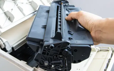 Ręka wyjmuje czarny toner z drukarki. Skorzystaj z naszej oferty bezpłatny odbiór tonerów.