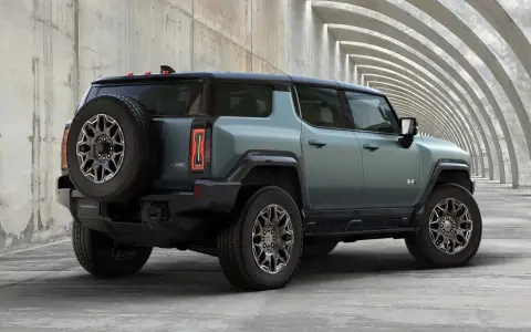 Zielony hummer elektryczny z kołem zapasowym z tyłu, zaparkowany przy betonowej konstrukcji z łukami.