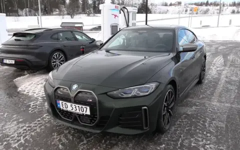 Zielony BMW i4 na ładowarce. W tle ciemny Porsche Taycan. Dane techniczne BMW i4 interesują wielu.
