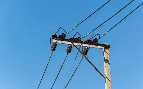 Słupy energetyczne z izolatorami ceramicznymi i przewodami pod napięciem. Brak zgody na służebność przesyłu może oznaczać problemy z infrastrukturą.
