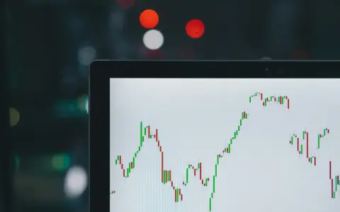 Wykres świecowy na ekranie laptopa pokazuje zmienność rynkową. W tle rozmyte światła, sugerujące noc i potencjalnie analizę rynków, np. rdn energia.