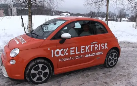 Pomarańczowy Fiat 500e w zimowej scenerii, z napisem "100% ELEKTRISK". Sprawdź zasięg tego elektryka!