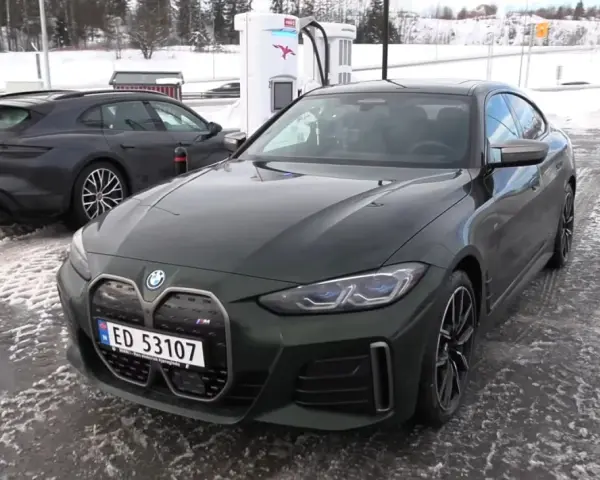 Zielony BMW i4 na ładowarce. W tle ciemny Porsche Taycan. Dane techniczne BMW i4 interesują wielu.