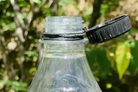 Nakrętki od butelek są przytwierdzone, by zapobiec ich zgubieniu i ułatwić ponowne zakręcenie. Widoczny fragment plastikowej butelki z otwartą, czarną nakrętką.